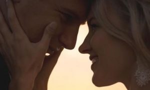 couple stands head to head looking smiling at each other