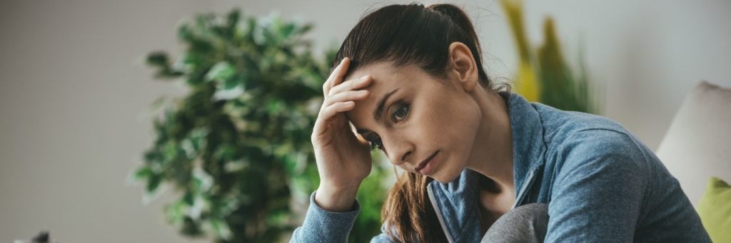 woman hand on forehead sitting on couch thinking