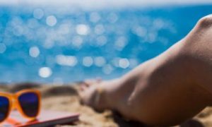 legs sunglasses book on sand beside blue ocean