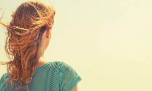 woman stands facing backward watching sunny sky