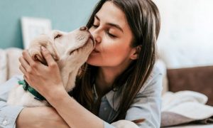 woman lies on bed hugging kissing puppy