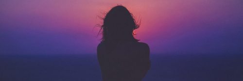 woman facing backward looks at purple blue red dark sky feeling lonely
