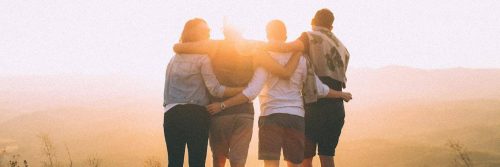 four people stands facing backward hugging watching sunset