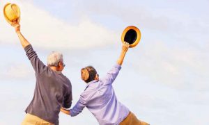 couple hand in hand stands backward raises hands holding yellow hat