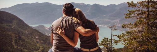 couple sits side by side on rock hugging enjoying happy moments in foggy weather on top of mountain