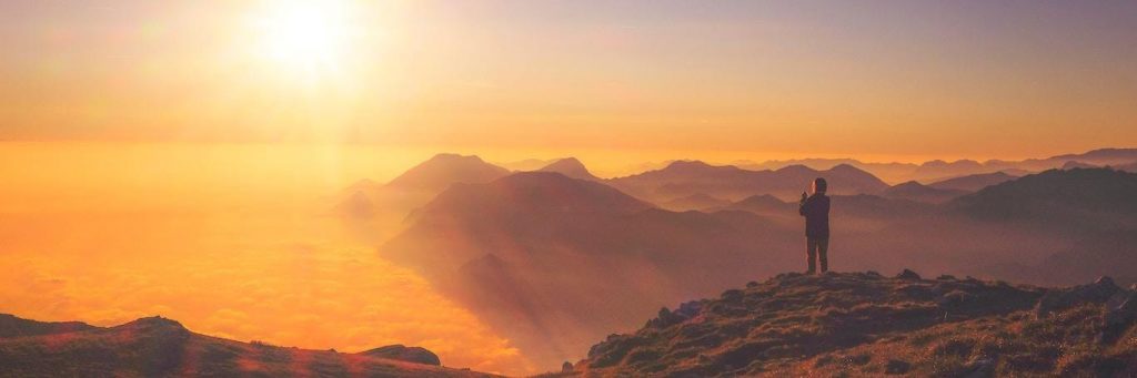 person stands on rock taking photos of beautiful sunny sky
