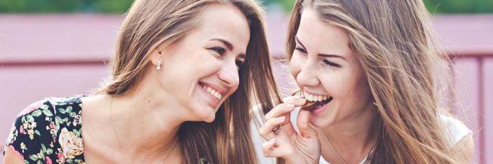 two women sits on bench talking laughing while one lady eating biscuit