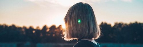short hair woman stands in forest looking at sunset