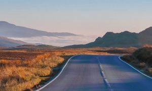 empty road approaching mountain between fields in cloudy sky