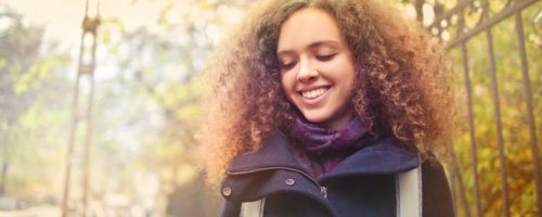 curly blonde hair woman looks down happily smiling next to fence in sunny sky