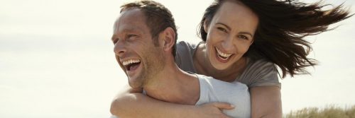 man excitedly carries girlfriend on back while woman happily laughing in cloudy sky