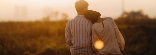 couple sits watching sunset while woman lying on partner shoulder