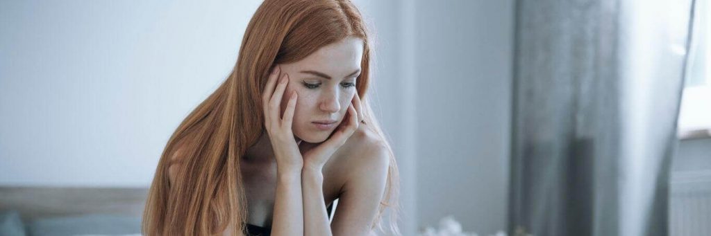 woman sad face hands on cheek sitting in bedroom thinking