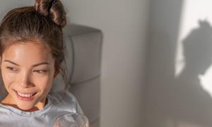 woman sits on bed holding glass of water smiling