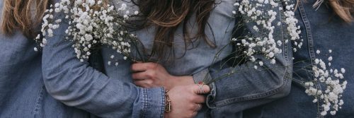 three women stands side by side holding white flowers