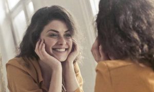 woman happily smiles looks herself in mirror