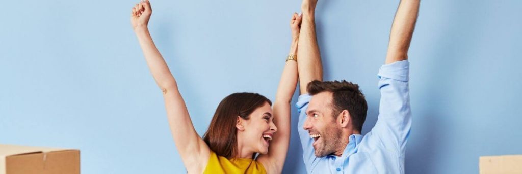 couple happily raises hands looking at each other blue wall