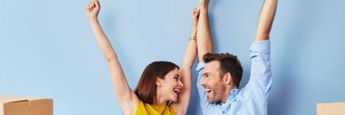 couple happily raises hands looking at each other blue wall
