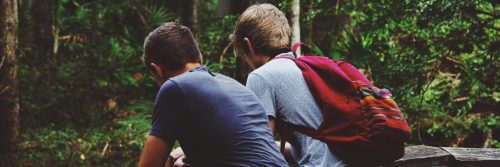 two men sits on bench in forest facing backward talking