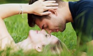 woman lies on field about to kiss boyfriend while man sitting head to head with her