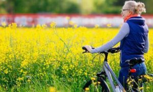 elderly woman walks on field with bicycle