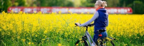 elderly woman walks on field with bicycle