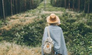 woman wearing back bag facing backward stands in forest