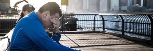man sits on bench near seaport hand in face feeling sad