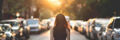 woman facing backward walks unconsciously between two lines of car traffic