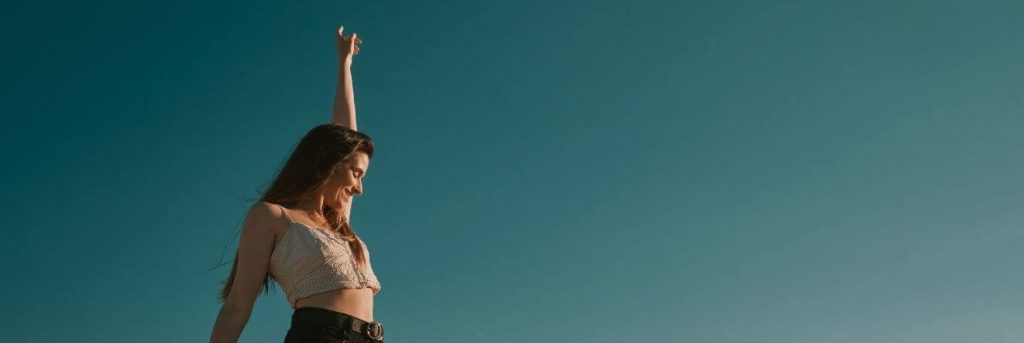 woman happily smiles raising hand in blue sky