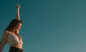 woman happily smiles raising hand in blue sky