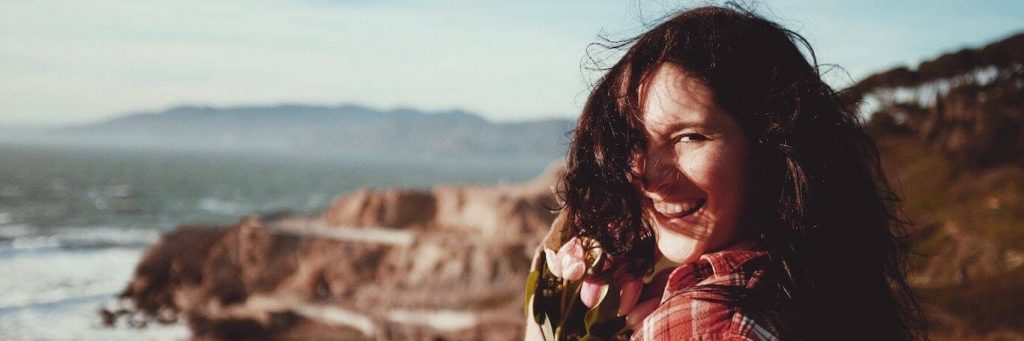 woman stands on rock smiling gratitude life in cloudy sky