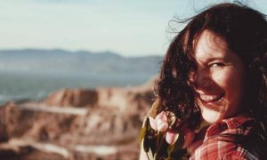 woman stands on rock smiling gratitude life in cloudy sky