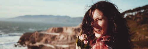 woman stands on rock smiling gratitude life in cloudy sky