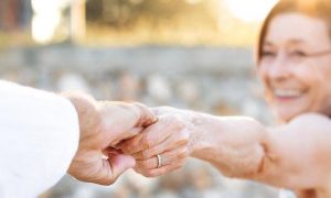 elderly woman happily smiles holding husband hand