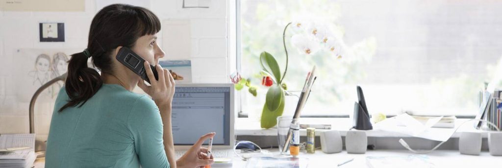 woman sits beside laptop plant pots sketch window answering call working from home
