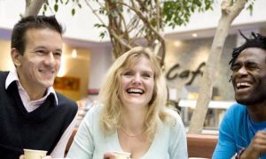 group of mixed genders sit next to coffee shop in shopping mall talking happily laughing