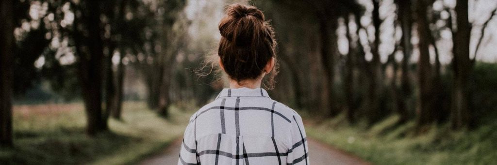woman facing backward stands on road between forest