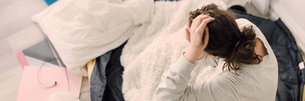 girl sits on bed touching hair warming up with white blanket