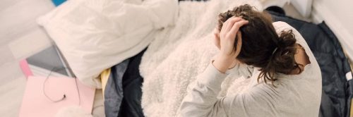 girl sits on bed touching hair warming up with white blanket