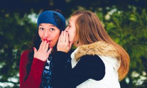 woman whispering to friend while lady surprises