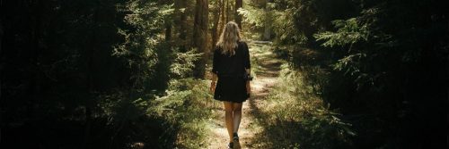 woman facing backward walks alone in forest