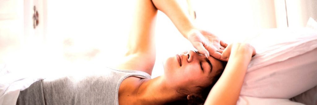 woman lies on bed hands on head closed eyes struggling to fall asleep