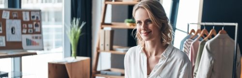 young woman with short blonde hair smiles board wooden drawer side table clothes hanging behind