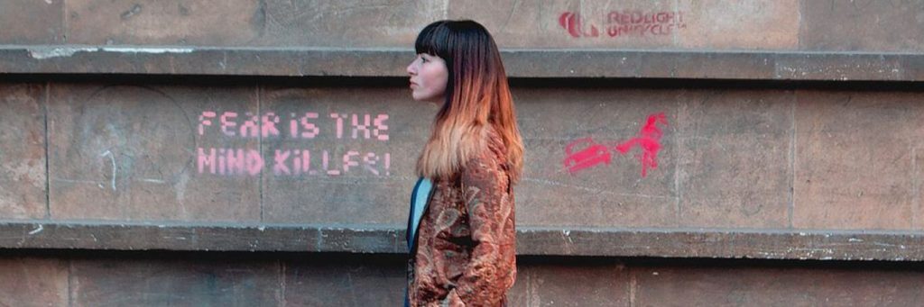 woman walks on street beside wall having pink gravity detailing fear is the mind killer
