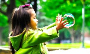 adorable girl wearing green coat happily excitedly plays with bubbles in park