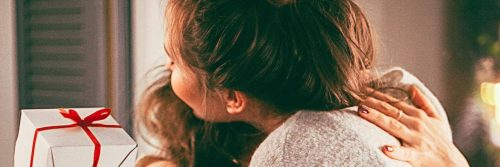 women hugging beside white christmas present wrapped by red banner