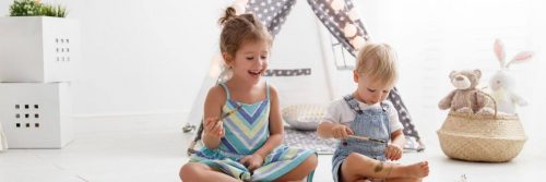 two adorable naughty children sits in living room painting on hands beside toys teddy bear