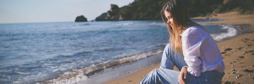 woman sits on sand beside beach feeling sad after relationship breakup