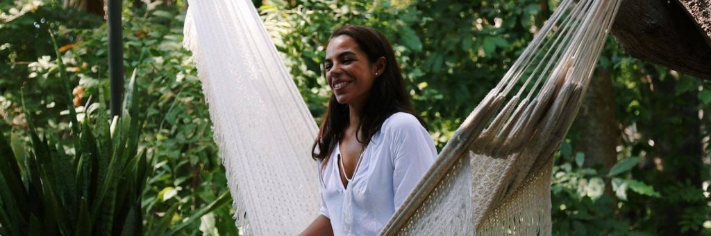 woman sits on white hammock happily smiling in forest
